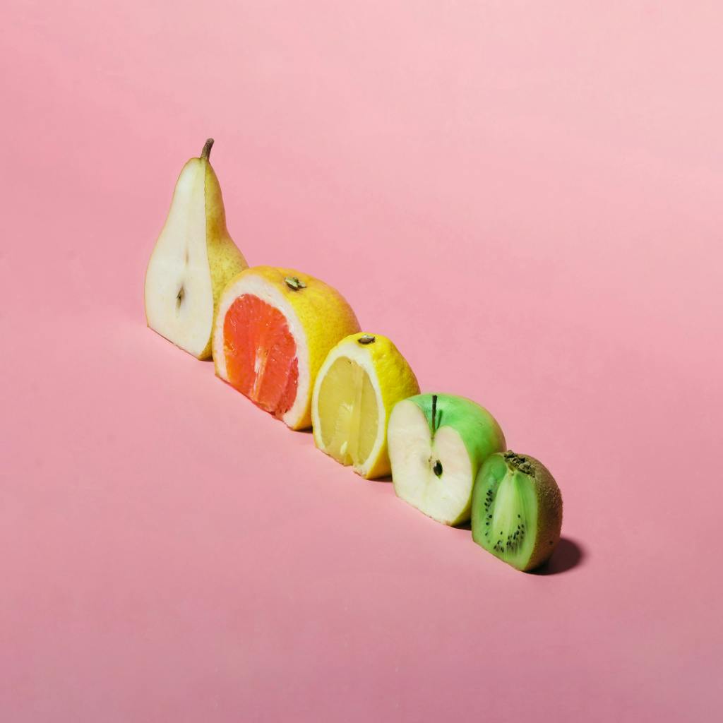 Valuing a business with inconsistent earnings - mixed fruit [pear, grapefruit, lemon, apple, kiwi] lined up on a pink background to illustrate inconsistency.