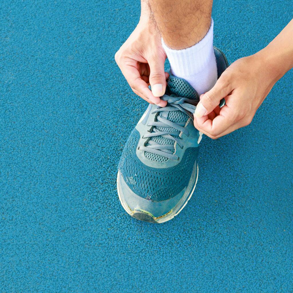Person tying a running shoe on a blue track, representing EOFY SMSF tips and financial preparation before 30 June.