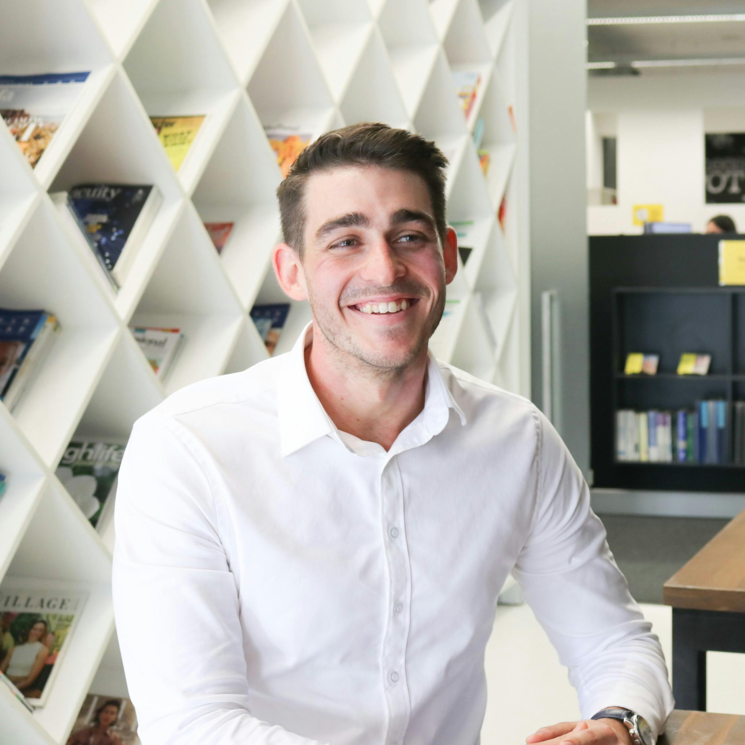 Photo of Ben Whittaker in white shirt smiling in front of book shelf